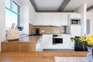 Una cocina moderna con armarios blancos, horno de acero inoxidable, microondas y encimera de madera.