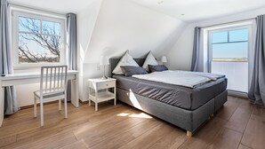 Quarto com cama, escrivaninha, cadeira e janela.