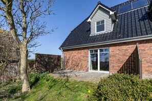 Une maison d’habitation avec une façade en briques, un toit en tuiles et une grande porte d’entrée en verre.