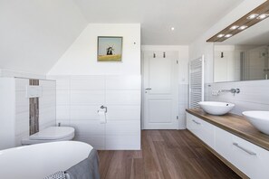 Une salle de bain moderne équipée d’une baignoire, de deux lavabos, de toilettes et d’une douche.