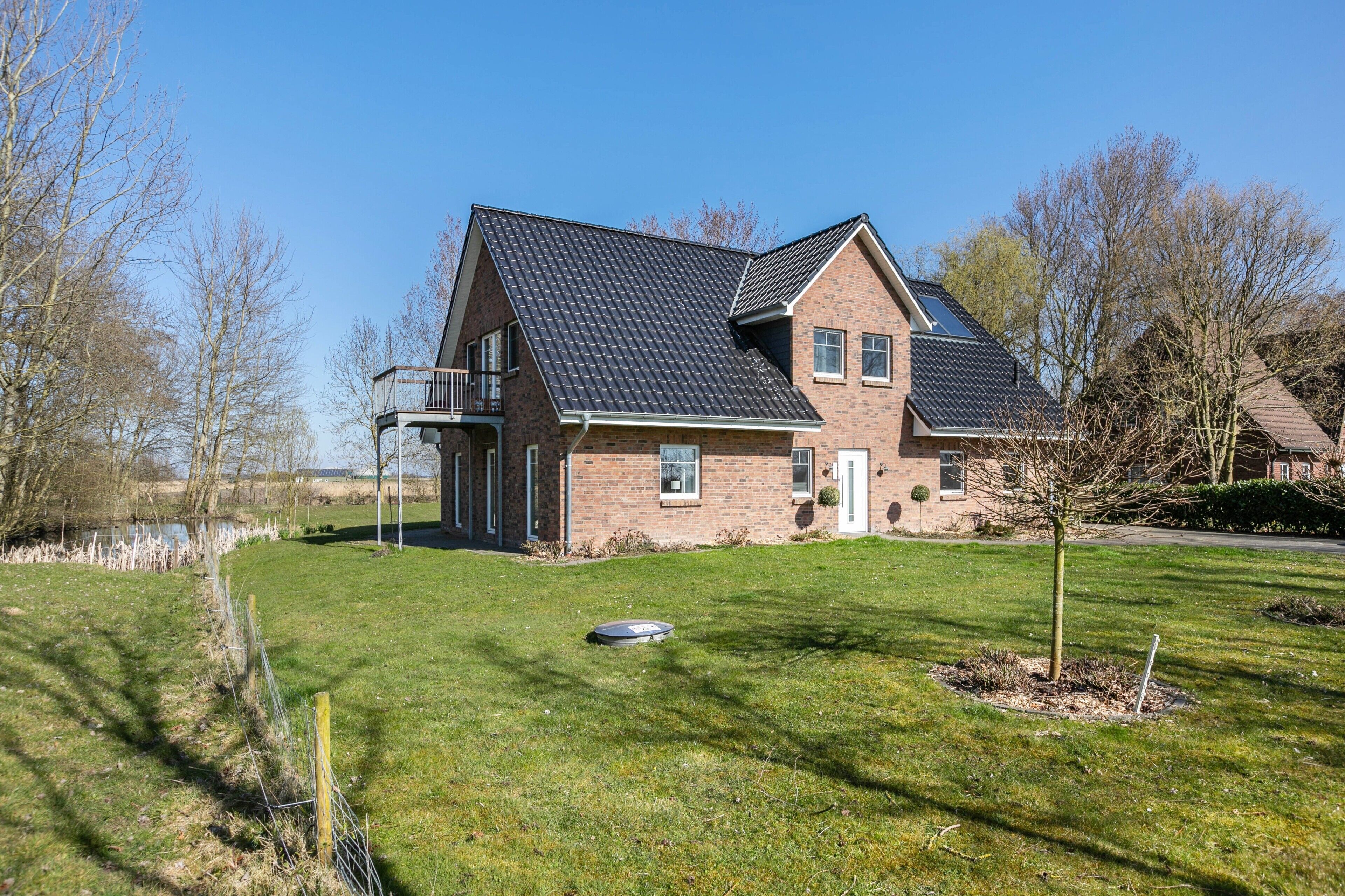 Une maison à deux étages, avec une façade en briques, un toit en pente et un petit balcon au deuxième étage.