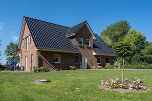 Une maison à deux étages, avec une façade en briques, un toit recouvert de tuiles sombres et une pelouse bien entretenue agrémentée de fleurs.