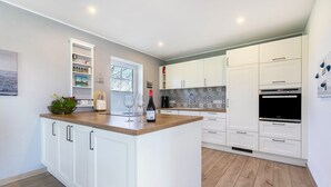 Una cocina moderna con armarios blancos, encimera de madera y un refrigerador para vinos empotrado.