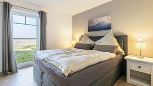 Un dormitorio con una cama grande, una mesita de noche con lámpara, una ventana con cortinas y un cuadro en la pared.