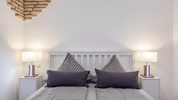 Una cama doble con ropa de cama a rayas, dos lámparas de noche y un cabecero blanco.