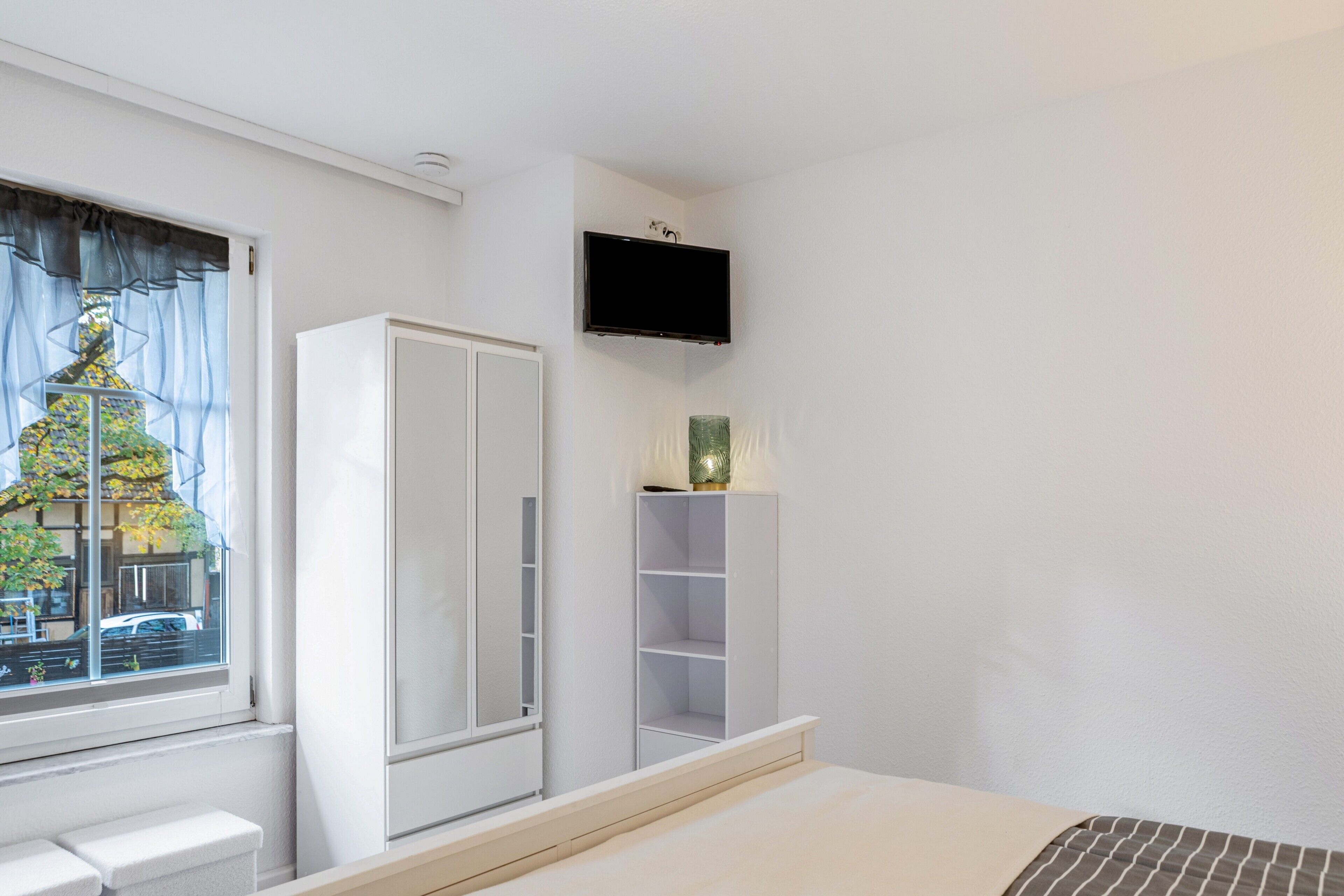 Une chambre à coucher comprenant un lit, une armoire, un téléviseur et une fenêtre donnant sur un immeuble.
