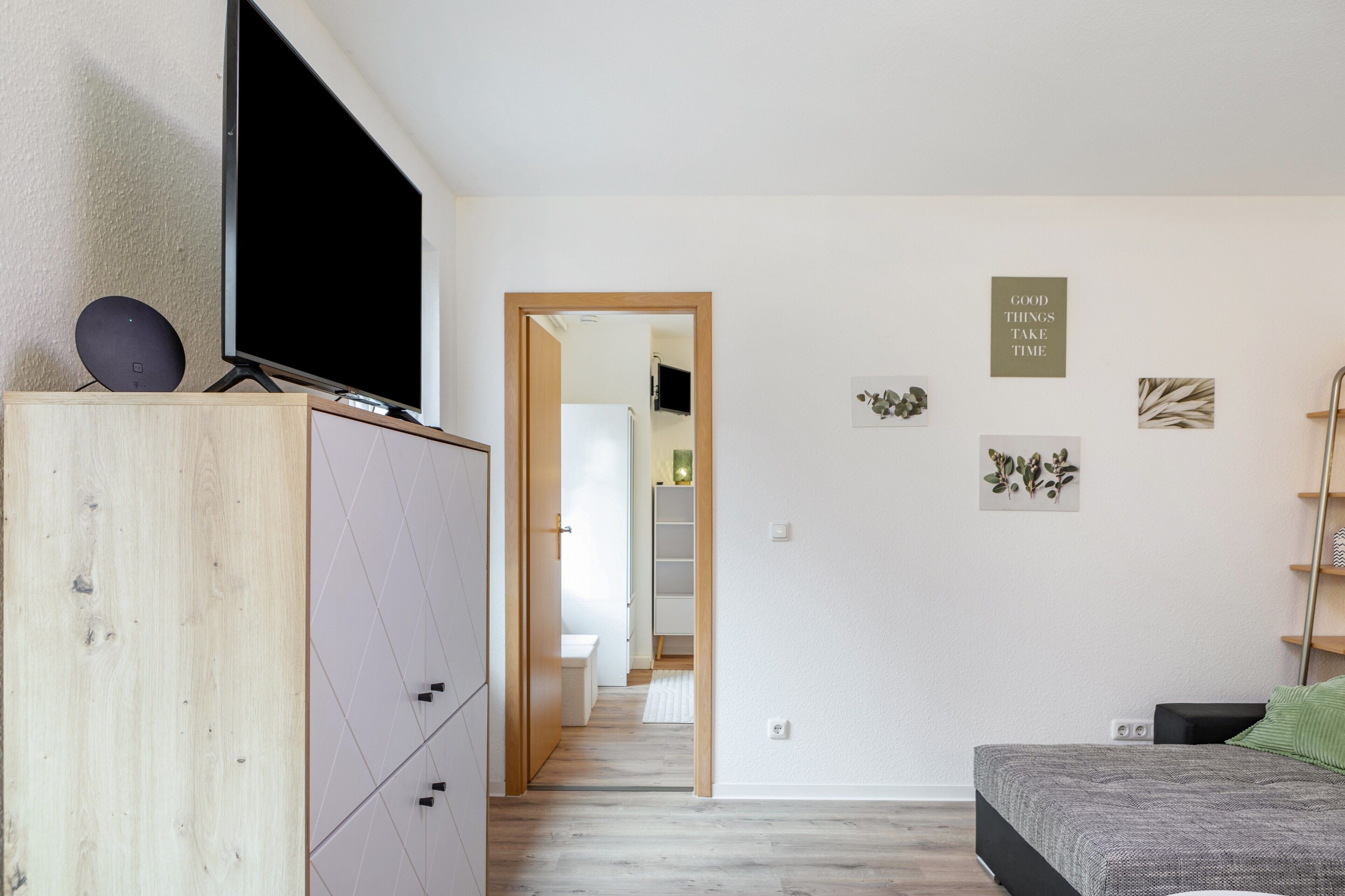 Ett sovrum med en säng, en tv på ett tv-bord, en garderob och en hall som leder till ett badrum.