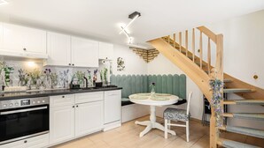 Una cocina moderna con armarios blancos, horno empotrado, una mesa de comedor con banco y una escalera de madera.