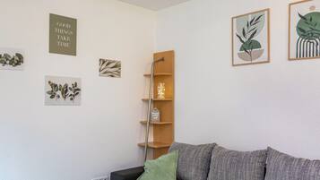 Een slaapkamer met een bed, een groen kussen, een houten plank met decoratieve objecten en wanddecoratie.