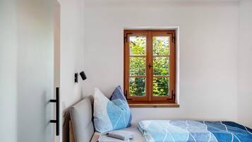 Une pièce avec un lit, une fenêtre et un luminaire fixé au mur.