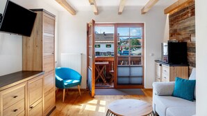 A room with a wooden ceiling, a television, a blue chair, a sofa, and a view through a door. - Room 'Apartment Mit Bergblick' with Mountain View, Balcony and Wi-Fi (Krün)