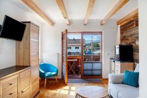 Une pièce avec un plafond en bois, une télévision, une chaise bleue, un canapé et une vue sur l’extérieur, visible à travers une porte.
