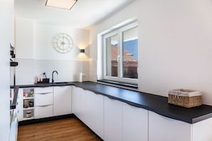 Una cocina moderna con armarios blancos, una encimera negra, un reloj y una ventana con vistas a edificios.