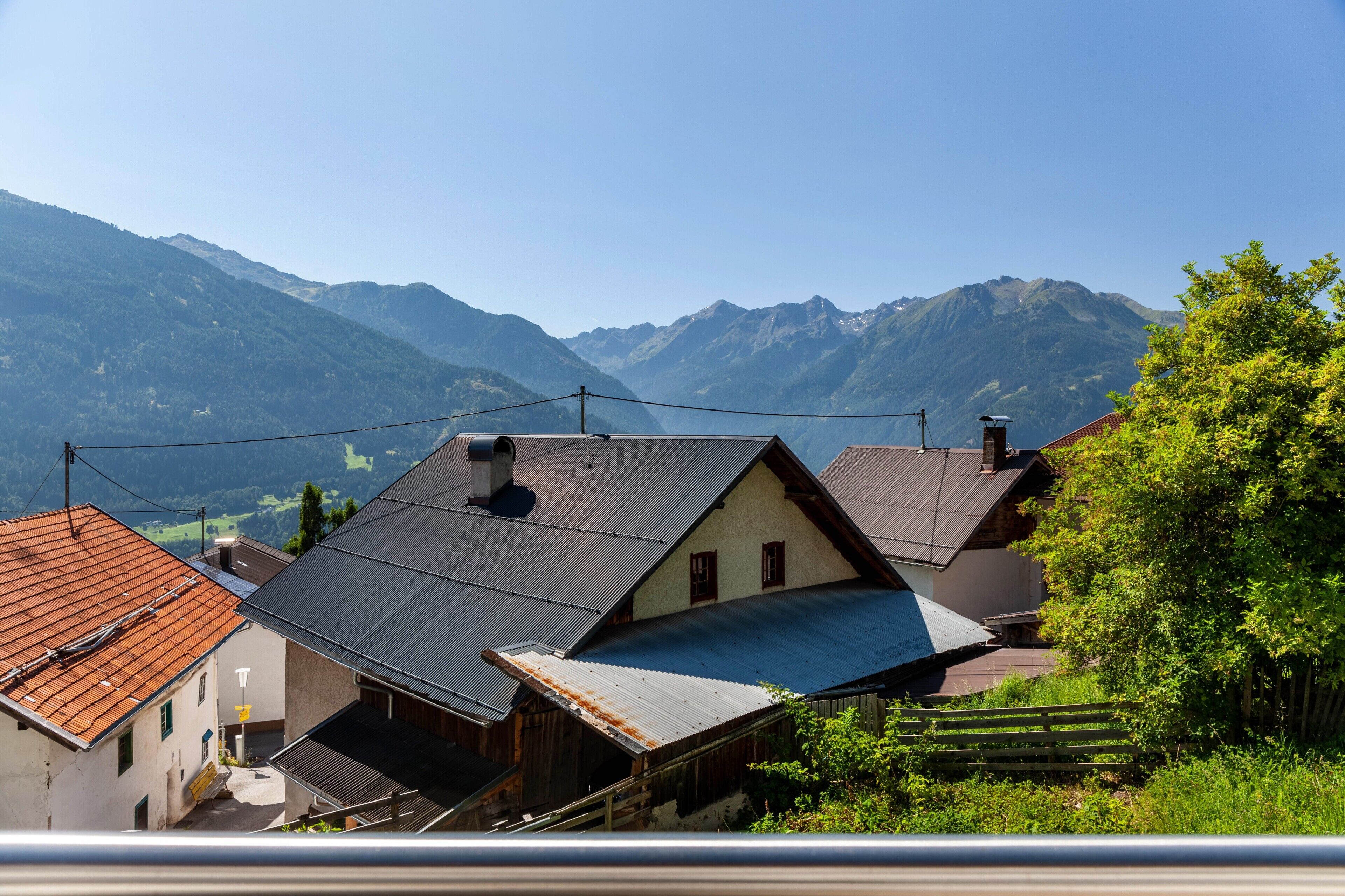 Un village de montagne aux maisons traditionnelles, doté d’une clôture en bois et offrant une vue dégagée sur les montagnes environnantes.