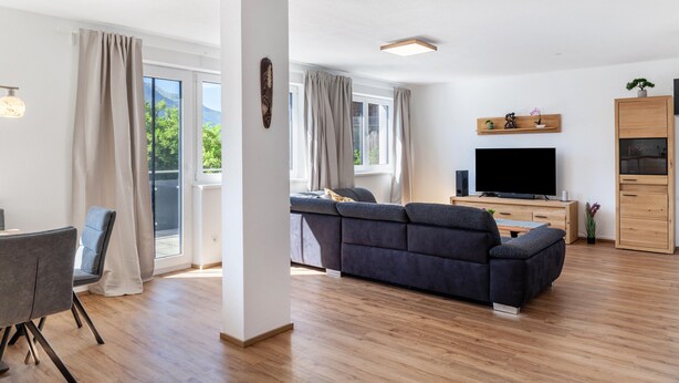 Een moderne woonkamer met een bank, televisie, houten kast en een eethoek met tafel en stoelen.
