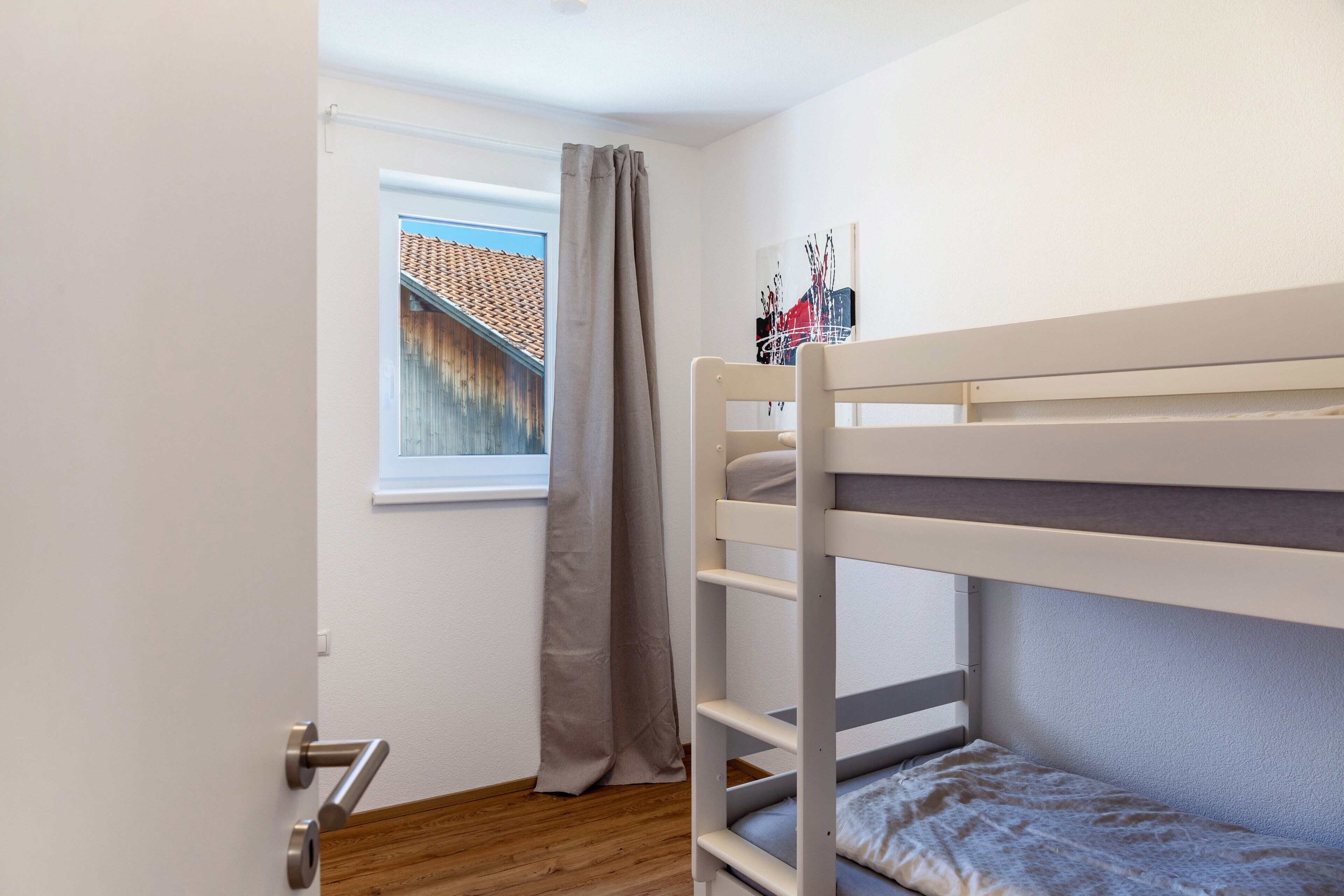Un lit superposé dans une pièce avec une fenêtre, un rideau et une porte.