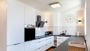 Een moderne keuken met witte kastjes, een zwart aanrecht, een magnetron, een koffiezetapparaat en een klok aan de muur.