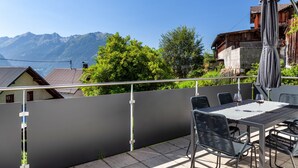 Een balkon met een tafel en stoelen, uitzicht op bergen en een gebouw met houten architectuur.