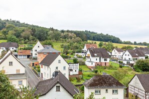 Un quartier résidentiel avec des maisons, une rue et une colline bordée d’arbres en arrière-plan.