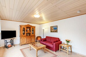 Olohuone, jossa on televisio, puinen kaappi, punainen sohva ja seinällä taulu.