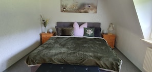 Een slaapkamer met een bed, twee nachtkastjes, een vaas met bloemen, een schilderij aan de muur en een radiator.