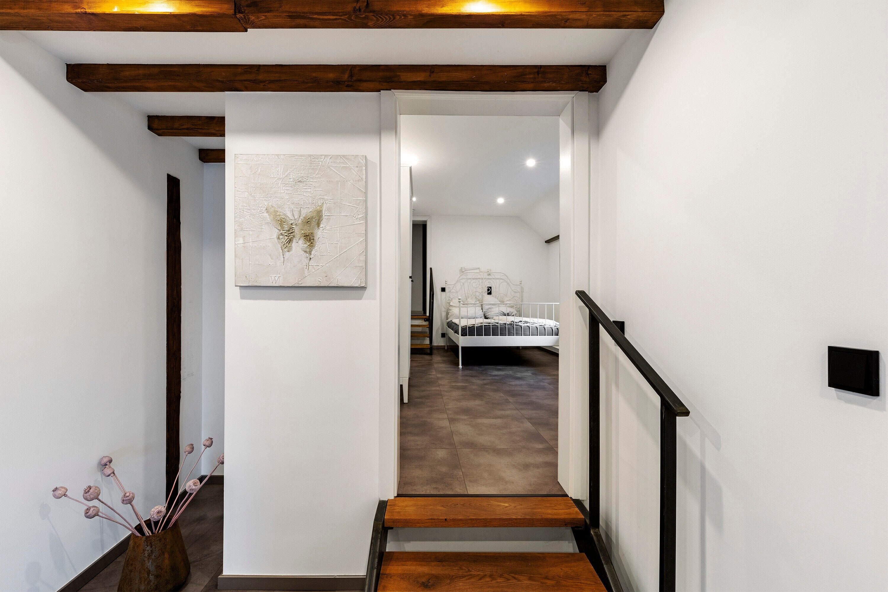 A staircase leading to a bedroom with a bed, a wall-mounted light, and a framed artwork.