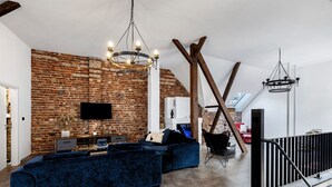 Un salon moderne avec un mur en briques, un grand canapé bleu, un téléviseur fixé au mur et un escalier doté d’une rampe.
