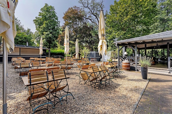 Espace extérieur aménagé avec des tables et des bancs, des parasols et un espace abrité avec une tonnelle.