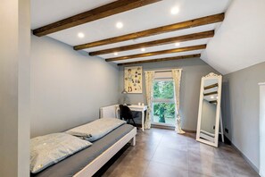 A bedroom with a bed, a desk, a chair, a mirror, and a window with curtains.