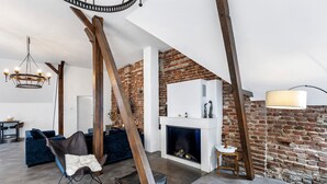Un salon de style industriel, avec des murs en briques apparentes, une cheminée, un lustre et des meubles modernes.