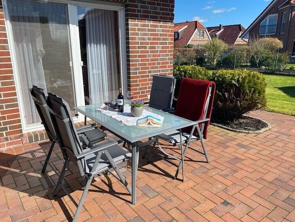 Un patio con una mesa de vidrio, dos sillas, una botella y un libro.