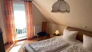 Una camera d'albergo con due letti, un comodino, una lampada, una sedia e vista sull'esterno.