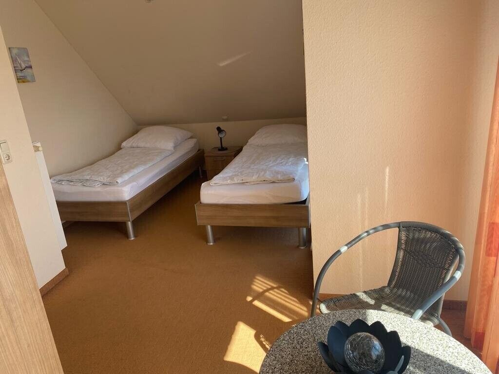 Eine kleine, einfache Unterkunft mit zwei Betten, einem Sessel und einem Tisch.