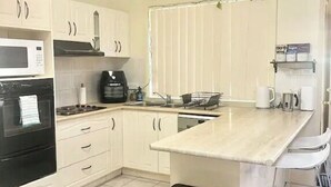 A modern kitchen with white cabinets, a black oven, a microwave, and a stainless steel trash bin.