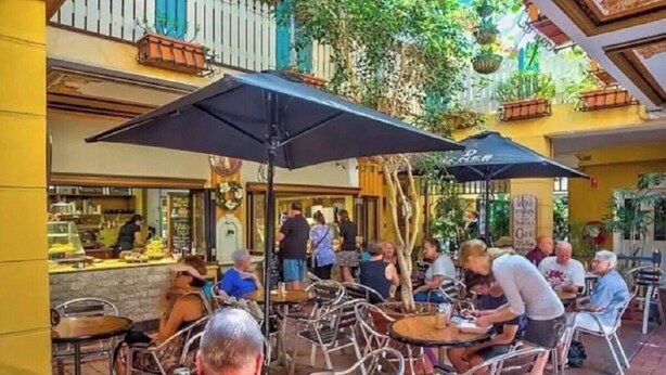 An outdoor café with metal chairs and tables, surrounded by yellow walls and potted plants.