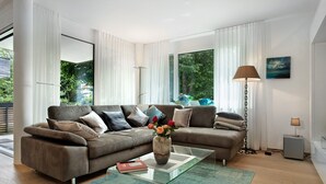 A modern living room with a sofa, a glass coffee table, a vase with flowers, a lamp, and a painting on the wall.