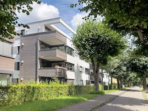 Ein modernes Mehrfamilienhaus mit Balkonen, einem gepflasterten Weg und umliegender Bepflanzung.