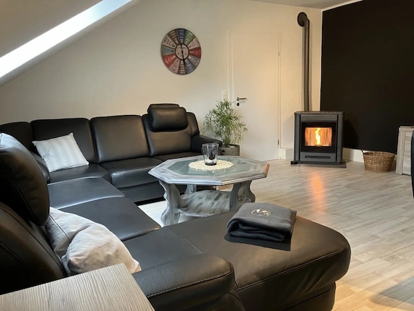 A modern living room with a sectional sofa, a glass coffee table, a wall clock, a fireplace, and a potted plant.