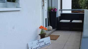 Eine weiße Außenwand mit einer Tür, einer Bank mit Kissen und einem Schild mit der Aufschrift 'Fewo Saverdlandherz'.