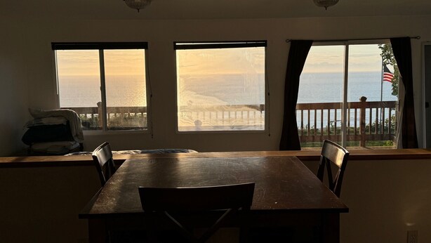 Ein Essbereich mit Holztisch und -stühlen, großen Fenstern mit Meerblick und einem Balkon mit Holzgeländer.