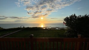 Sonnenuntergangblick von einer Terrasse mit Holzgeländer, mit Blick auf eine Wiese und den Ozean.