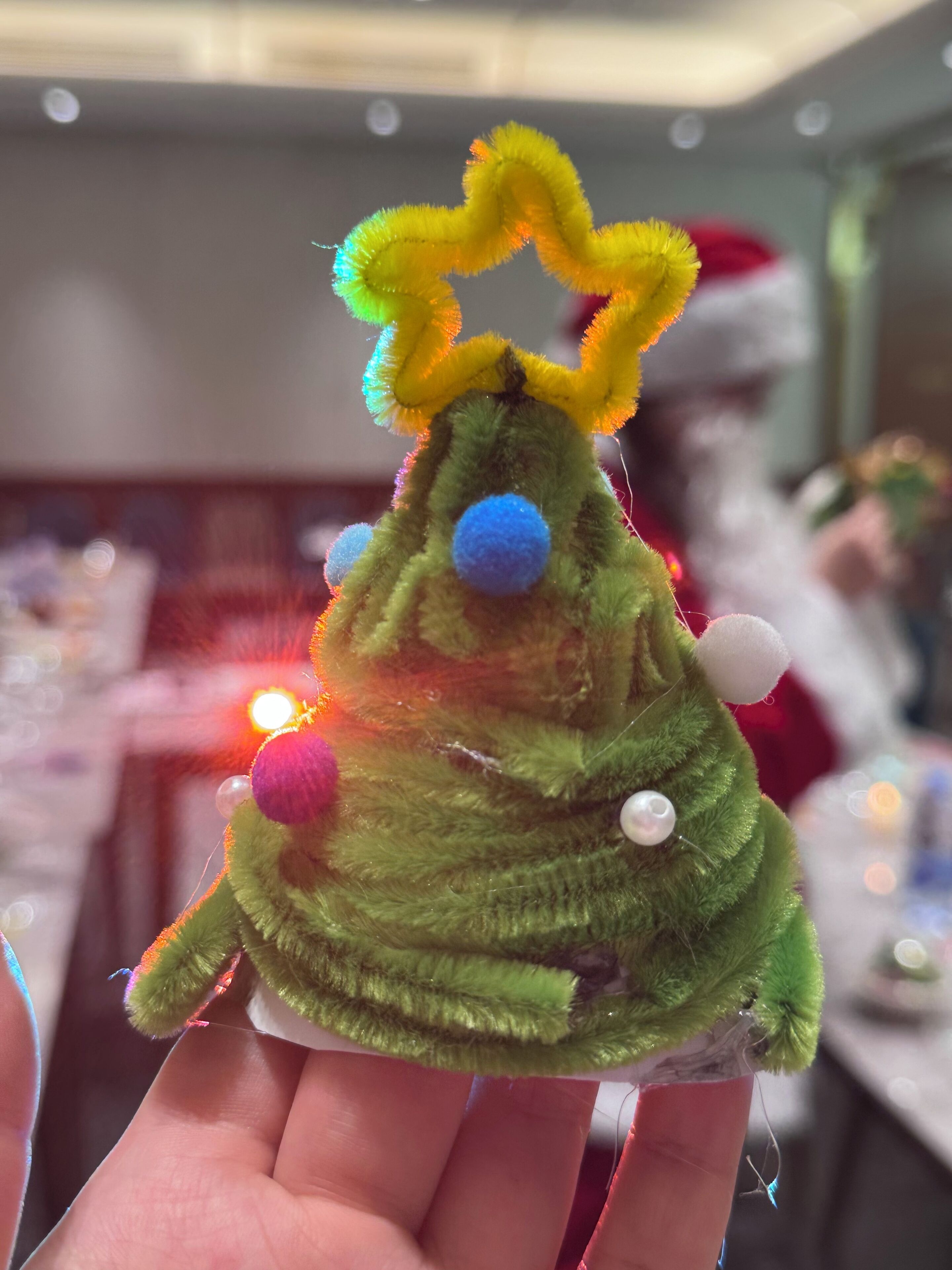 A hand holding a green plush toy with a yellow bow and pom-poms.