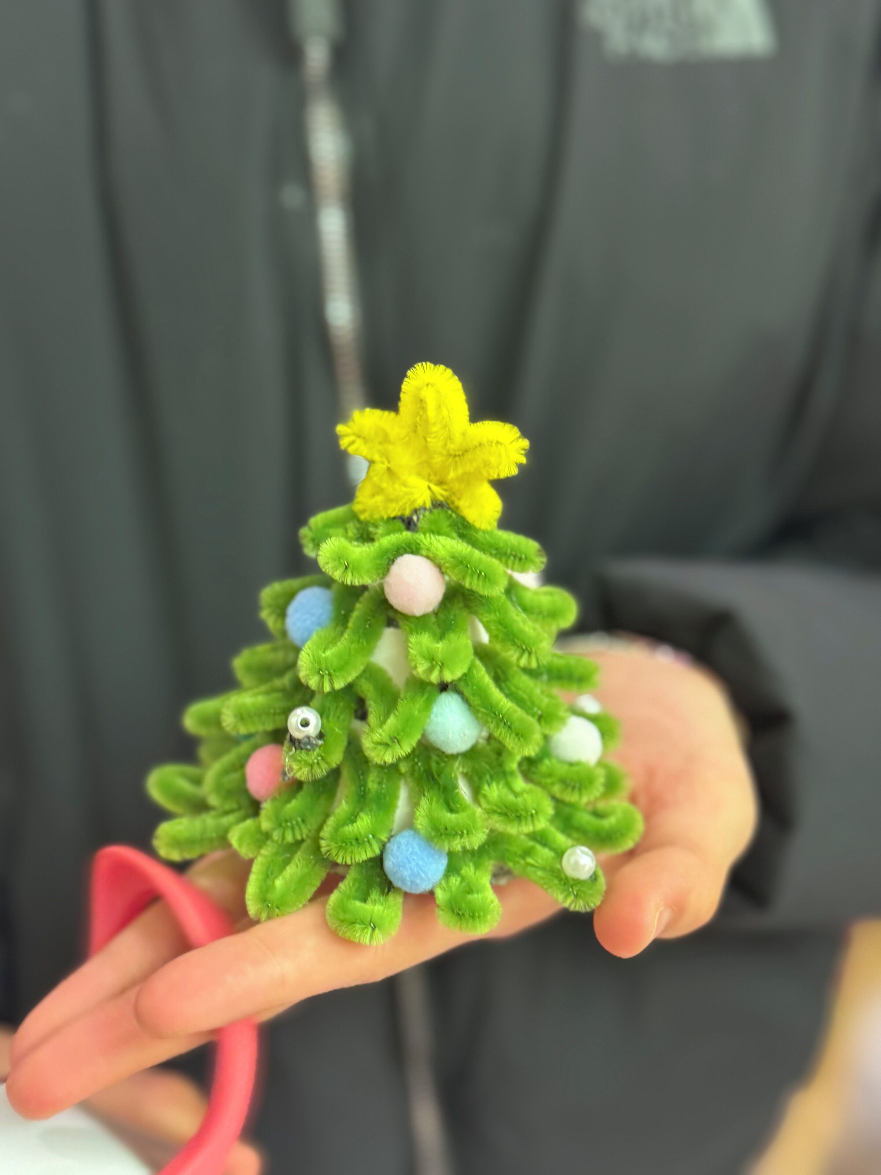 A hand holding a small, green, felt Christmas tree with colorful ornaments.