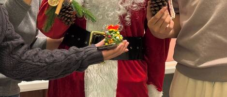 Una persona disfrazada de Papá Noel sosteniendo una caja de regalo pequeña y una piña con una campana.