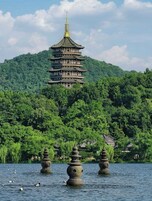 Una pagoda tradicional de varios niveles con un estripe dorado, rodeada de abundante vegetación y un lago tranquilo con faroles de piedra.