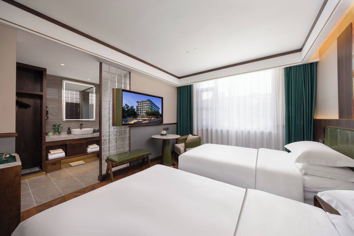 A hotel room with two beds, a bathroom with a sink and mirror, a small table, and a TV.