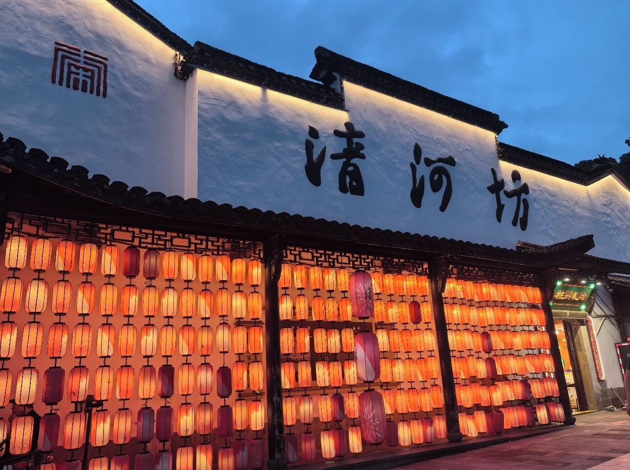 A traditional building with a sign in Chinese characters, multiple rows of hanging lanterns, and a tiled roof.