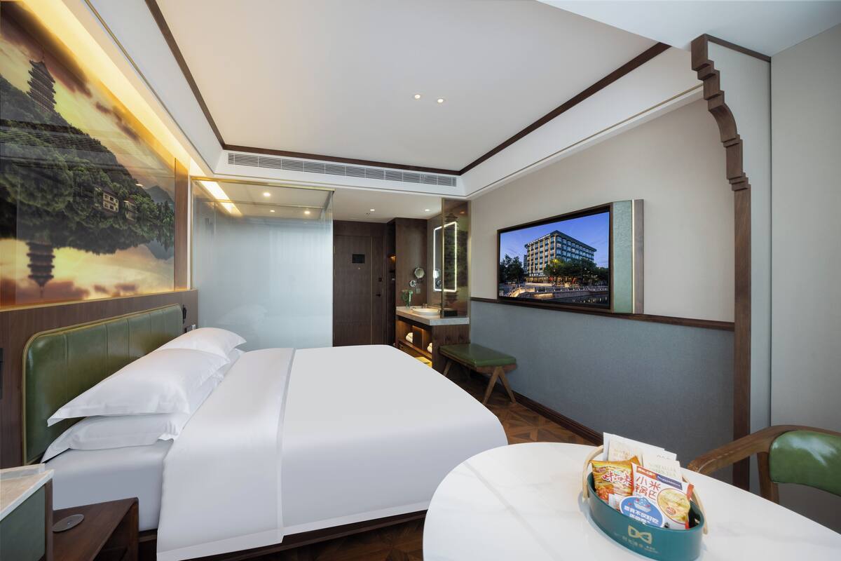 A hotel room with a bed, a desk, a chair, a television, and a wall-mounted mirror.