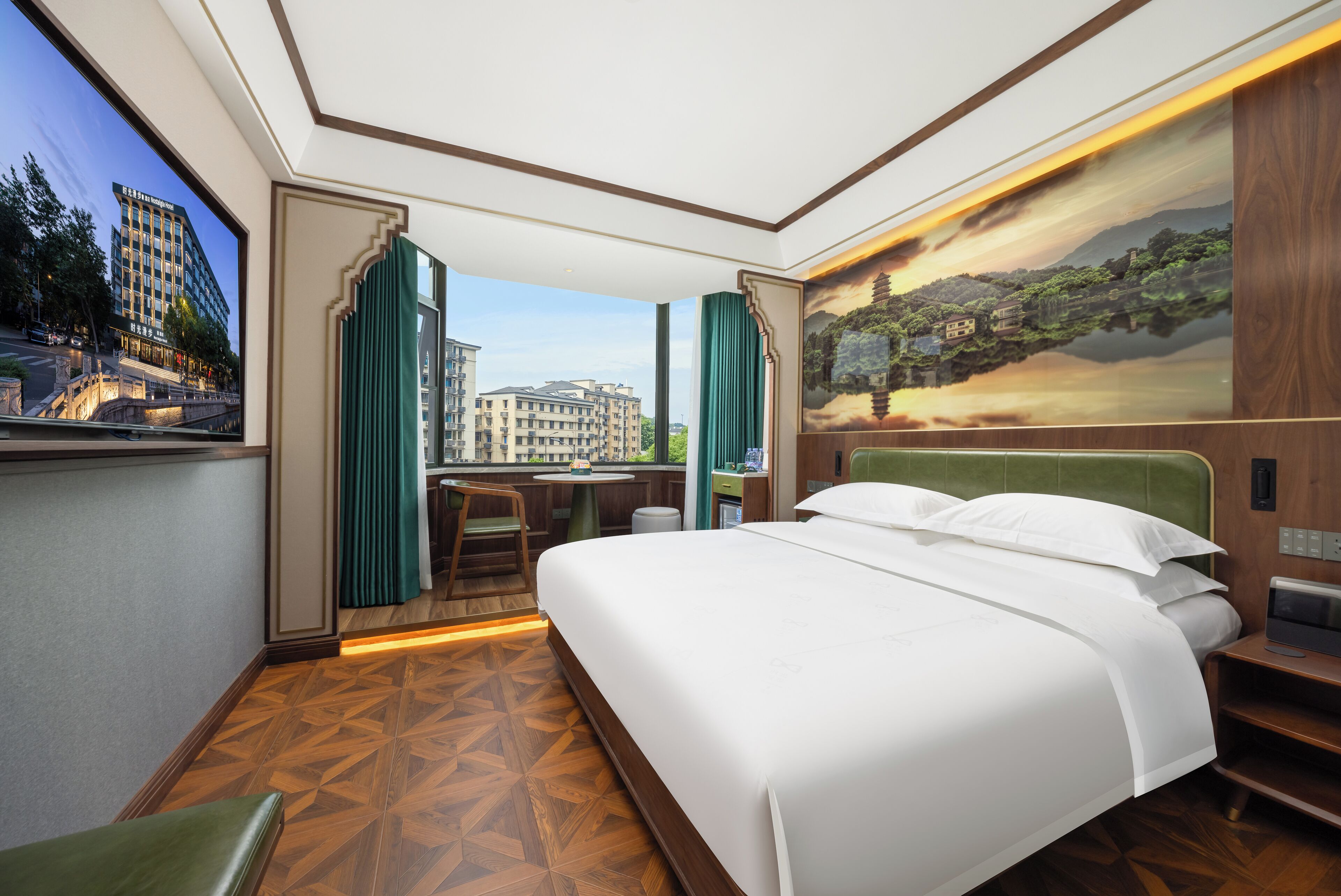 A hotel room with a large bed, a desk with a chair, a view of a cityscape through a window, and a painting of a landscape on the wall.