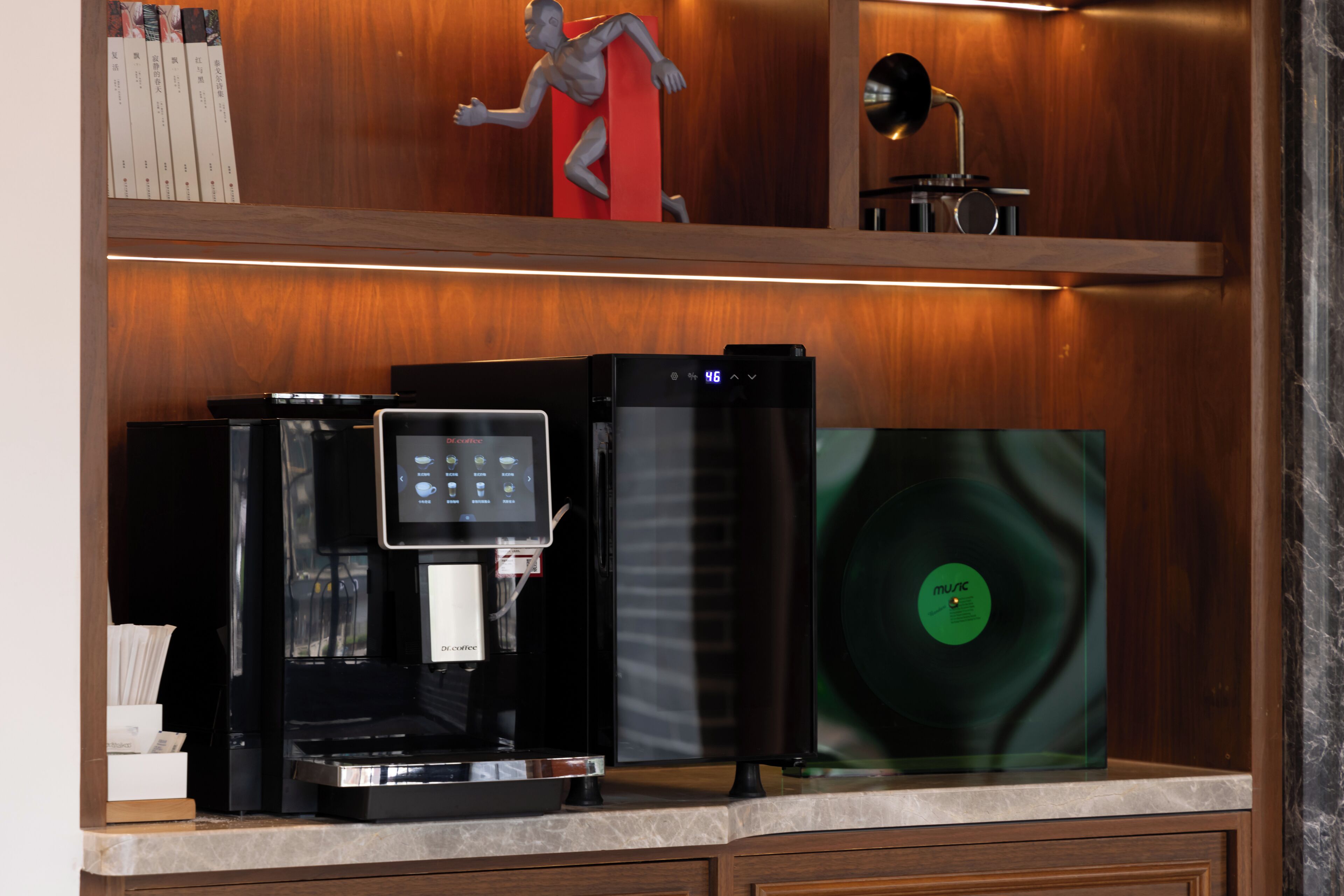 Una macchina da caffè con display digitale, un disco in vinile e una piccola statua su un ripiano in legno.